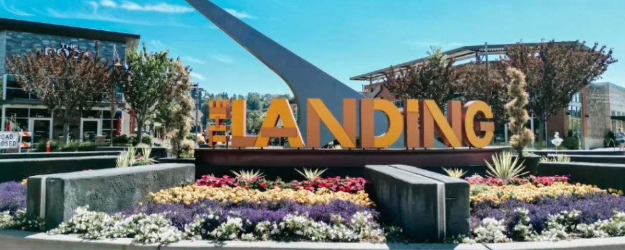 Ein großes Schild mit dem Wort 'LANDING' in Fettschrift, umgeben von einer begrünten Fläche mit verschiedenen Pflanzen und Blumen.