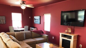 A living room with a sectional sofa, a coffee table, a flat-screen TV, a fireplace, and a ceiling fan.
