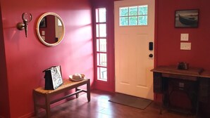 A hallway with a wooden bench, a mirror, a door with a window, and a small table with a basket.