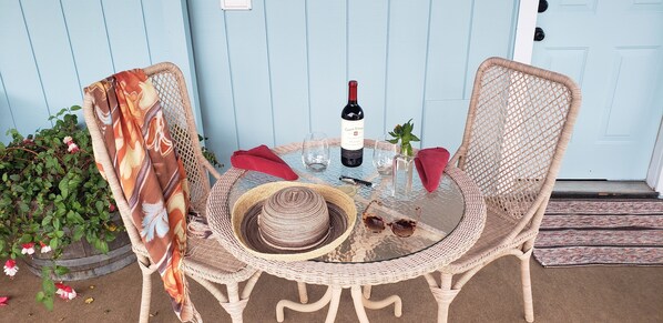 A wicker table set with a wine bottle, glasses, a hat, and sunglasses.