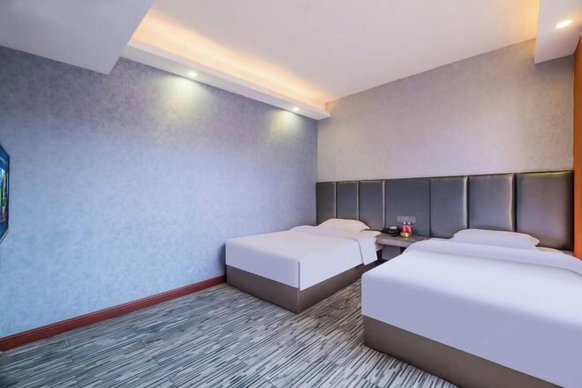 Ein Hotelzimmer mit zwei Betten, einem Nachttisch und einem an der Wand montierten Fernseher.