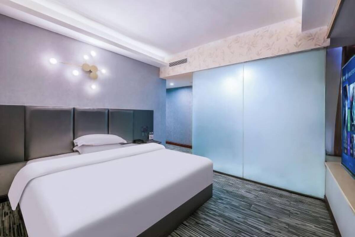 Ein Hotelzimmer mit einem großen Bett, einem Kopfteil, einem Flachbildfernseher und einem Kleiderschrank.