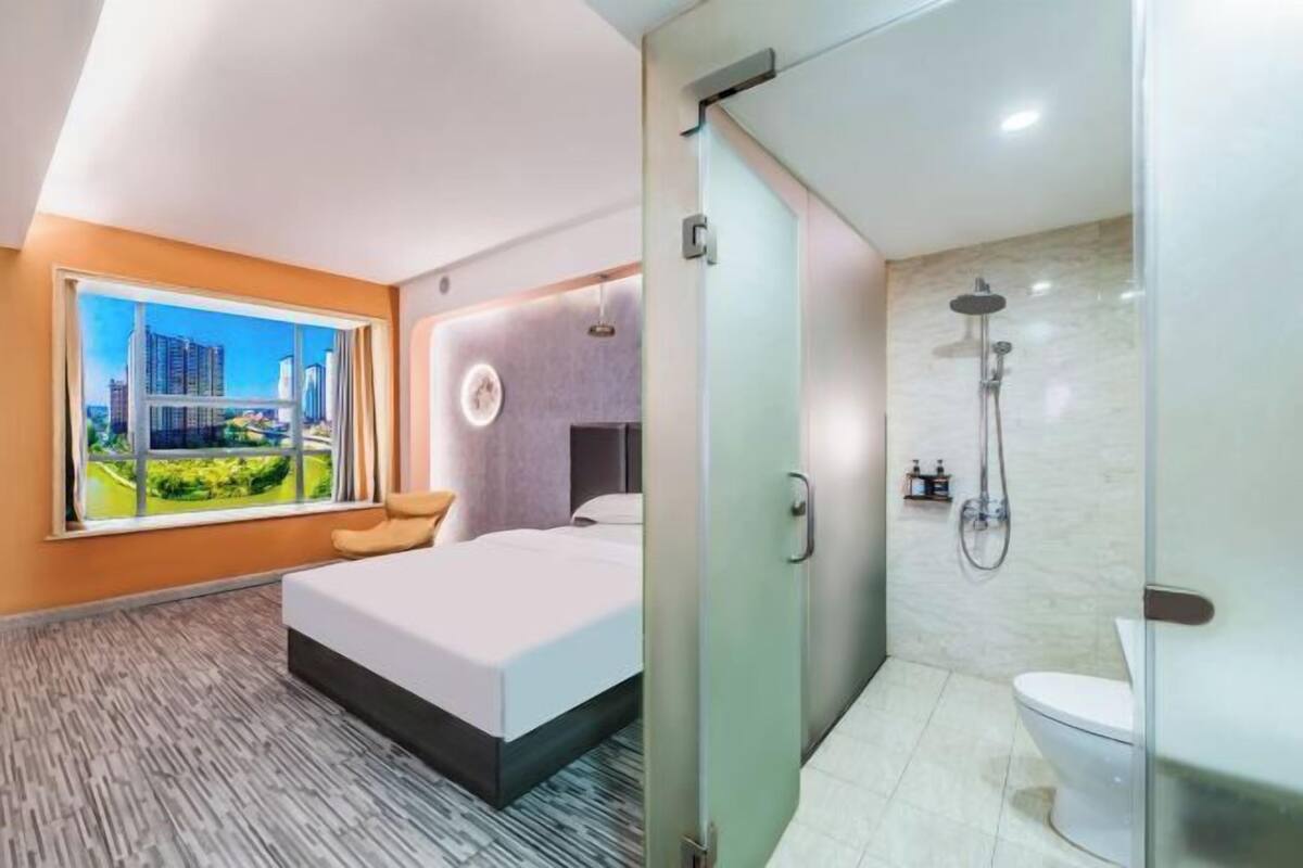 Ein modernes Hotelzimmer mit Bett, großem Fenster und Blick auf die Stadt, Dusche und Toilette.