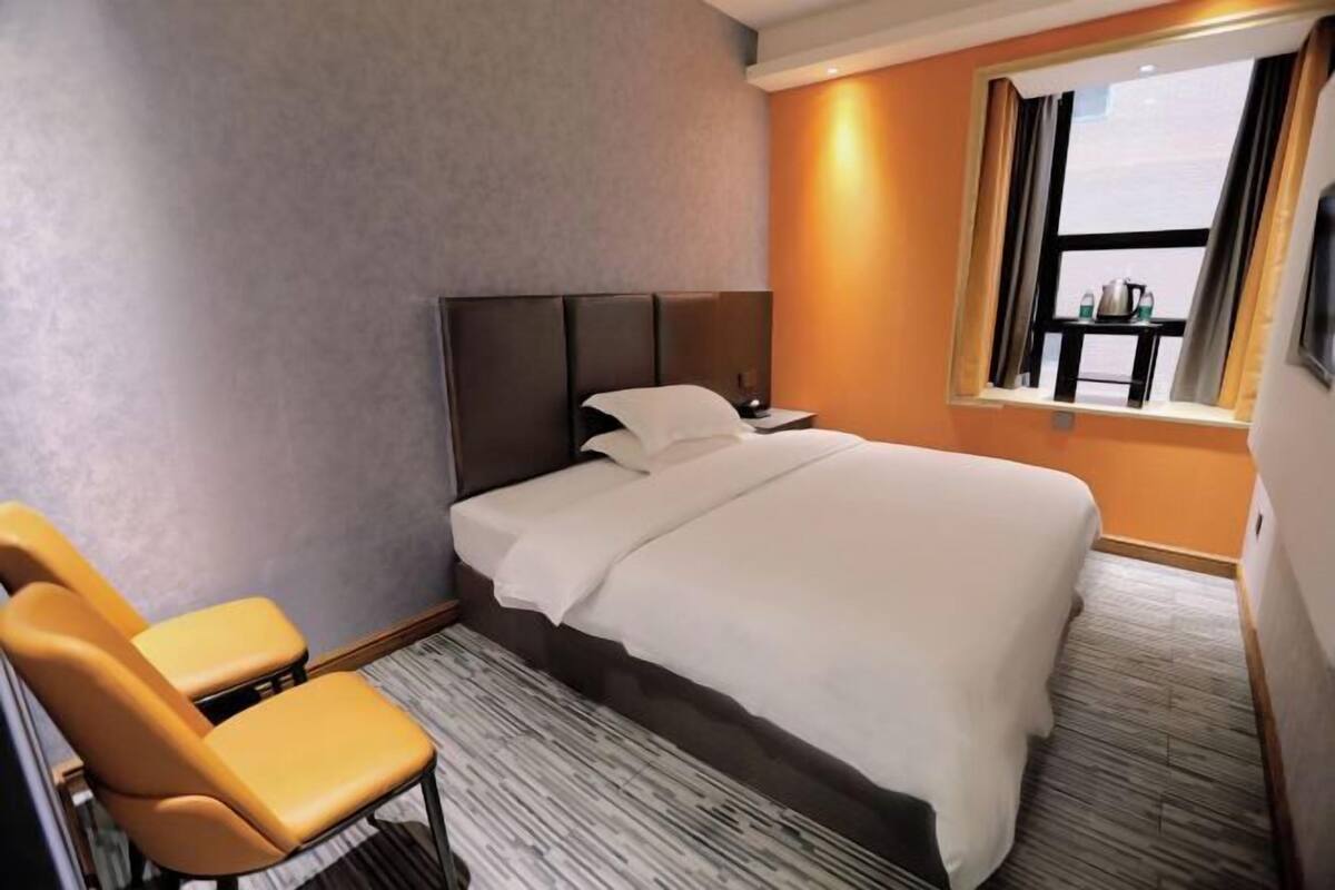 Ein Hotelzimmer mit Bett, zwei Stühlen, einem Nachttisch, einem Fenster mit Vorhängen und einem kleinen Tisch am Fenster.