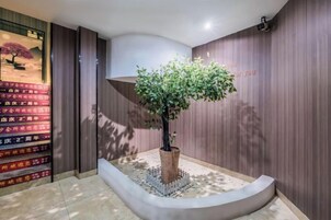Zona de recepción con una planta en maceta, un banco curvo y una pared con paneles de madera verticales.