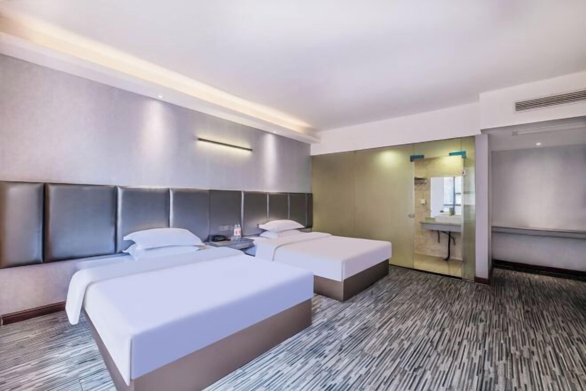 A hotel room with two beds, a large headboard, a walk-in closet, and a bathroom with a glass partition.