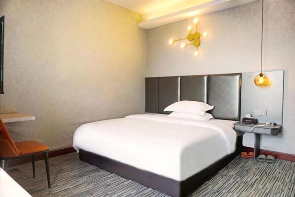 Une chambre d’hôtel avec un grand lit, une table de chevet avec une lampe, une chaise et un petit bureau avec une autre chaise.