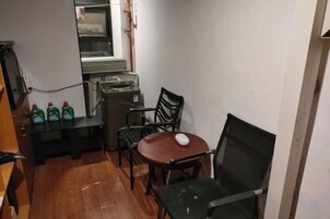 Una habitación pequeña con piso de madera, una mesa redonda con una silla, una silla negra, un ratón blanco y una pila de libros.