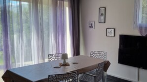Zona pranzo con tavolo, sedie, televisore e tende.