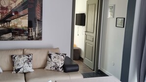 Un soggiorno moderno con un divano beige, due cuscini decorati, un televisore a schermo piatto e un grande quadro raffigurante un panorama urbano.