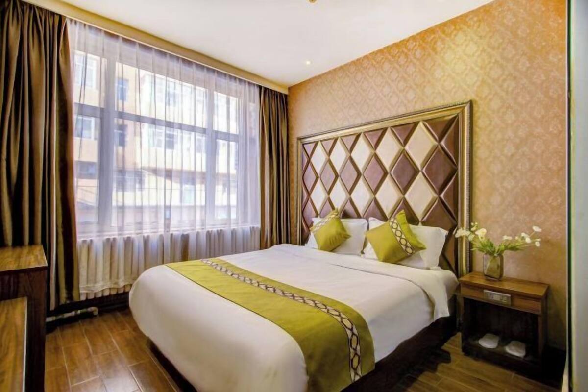 A hotel room with a large bed, a nightstand, a window with curtains, and a patterned wall.