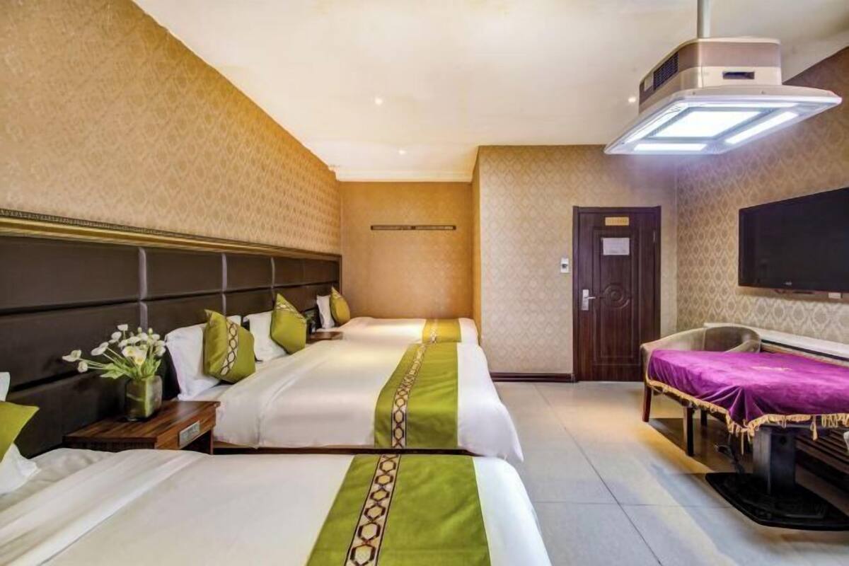 A hotel room with two beds, a desk, a flat-screen TV, and a ceiling-mounted air conditioner.