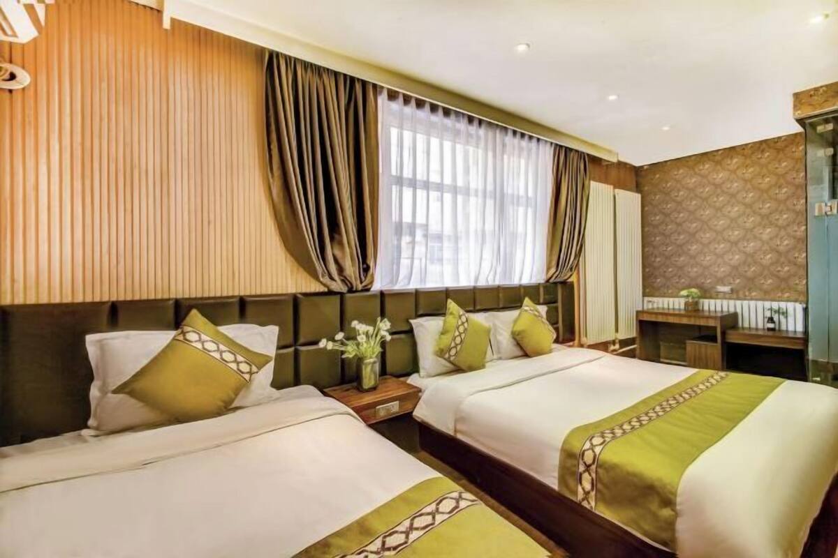 A hotel room with two beds, a desk, and a shower area.