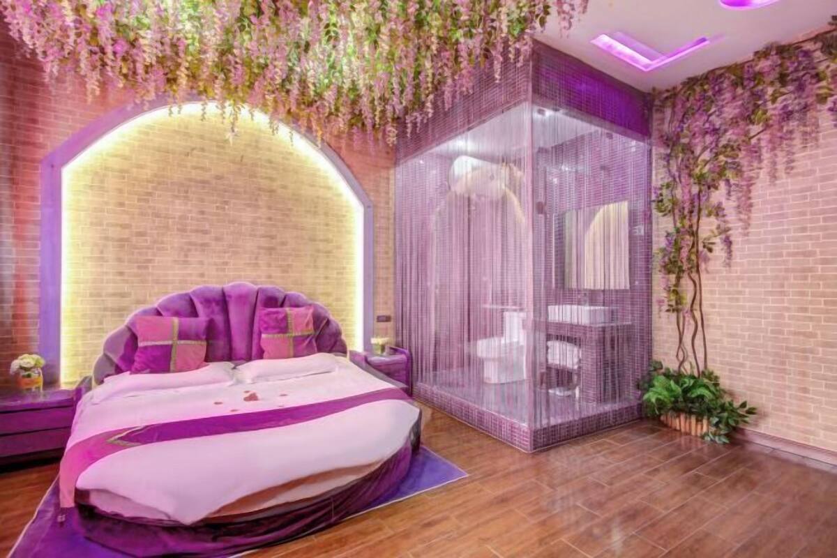 A modern bedroom with a large bed, a glass partition, and a brick wall.