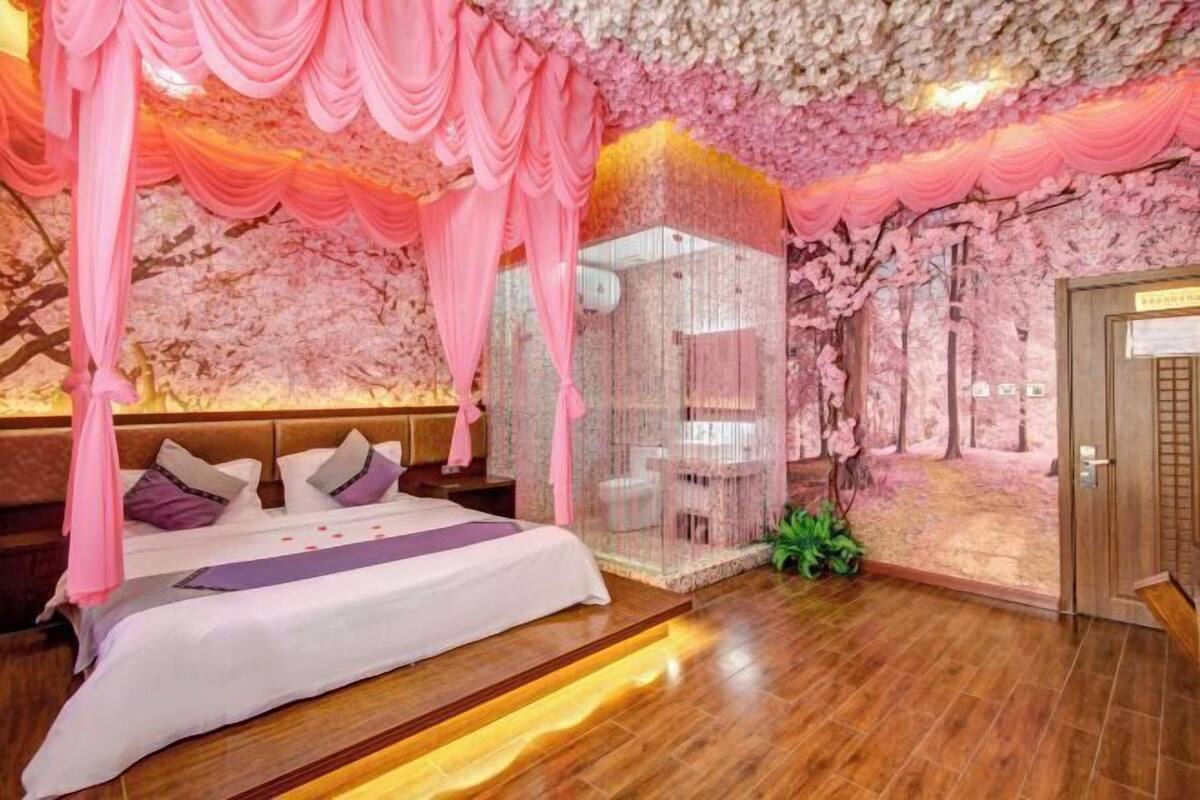 A bedroom with a canopy bed, a glass partition, and a wooden floor.