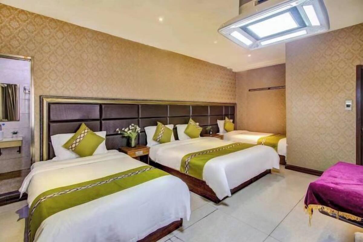 A hotel room with three beds, a large mirror, and a small table with a vase of flowers.