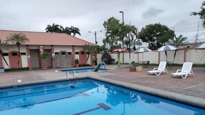 A swimming pool with clear blue water, surrounded by lounge chairs and a building with a red-tiled roof. - Cozy, secure and private suite  (Guayaquil)