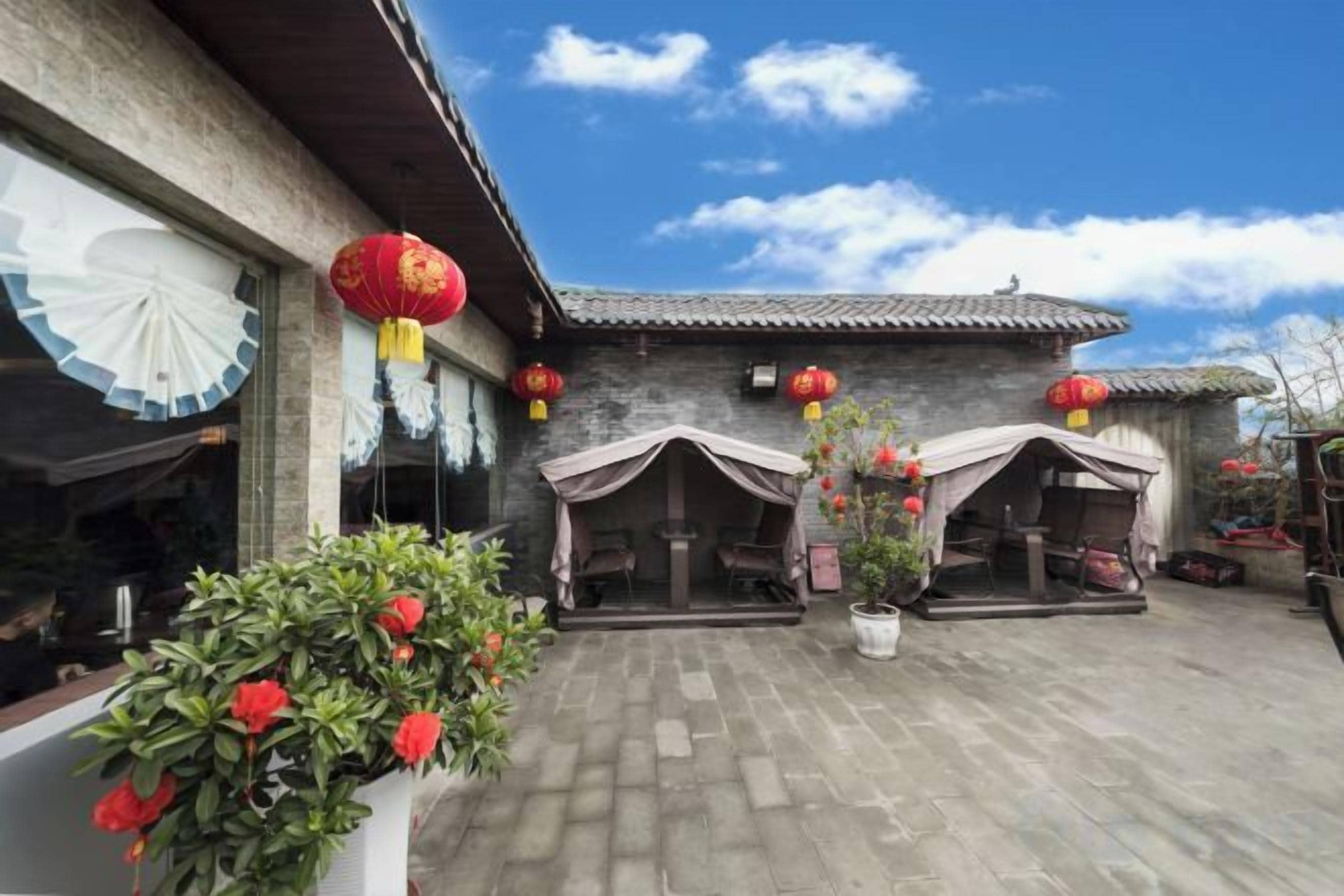 A courtyard with a traditional building, two covered seating areas, and potted plants.