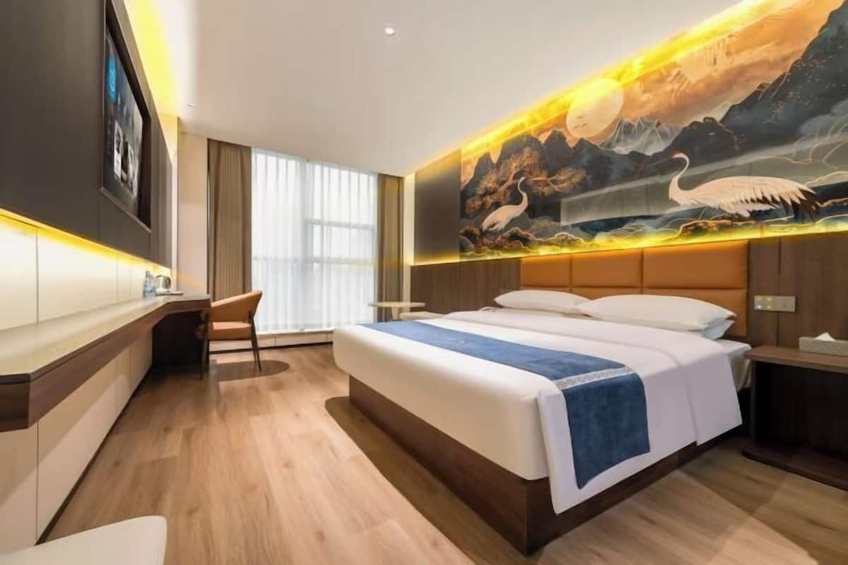 A modern hotel room with a large bed, a desk, and a wall mural.