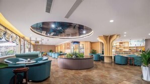 A modern lobby with a central circular seating area, a reception desk, and a view of the sea through large windows.