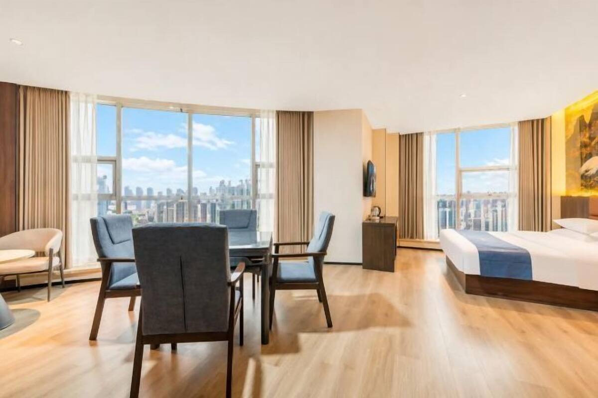 A modern hotel room with a city view, a dining area, and a large bed.