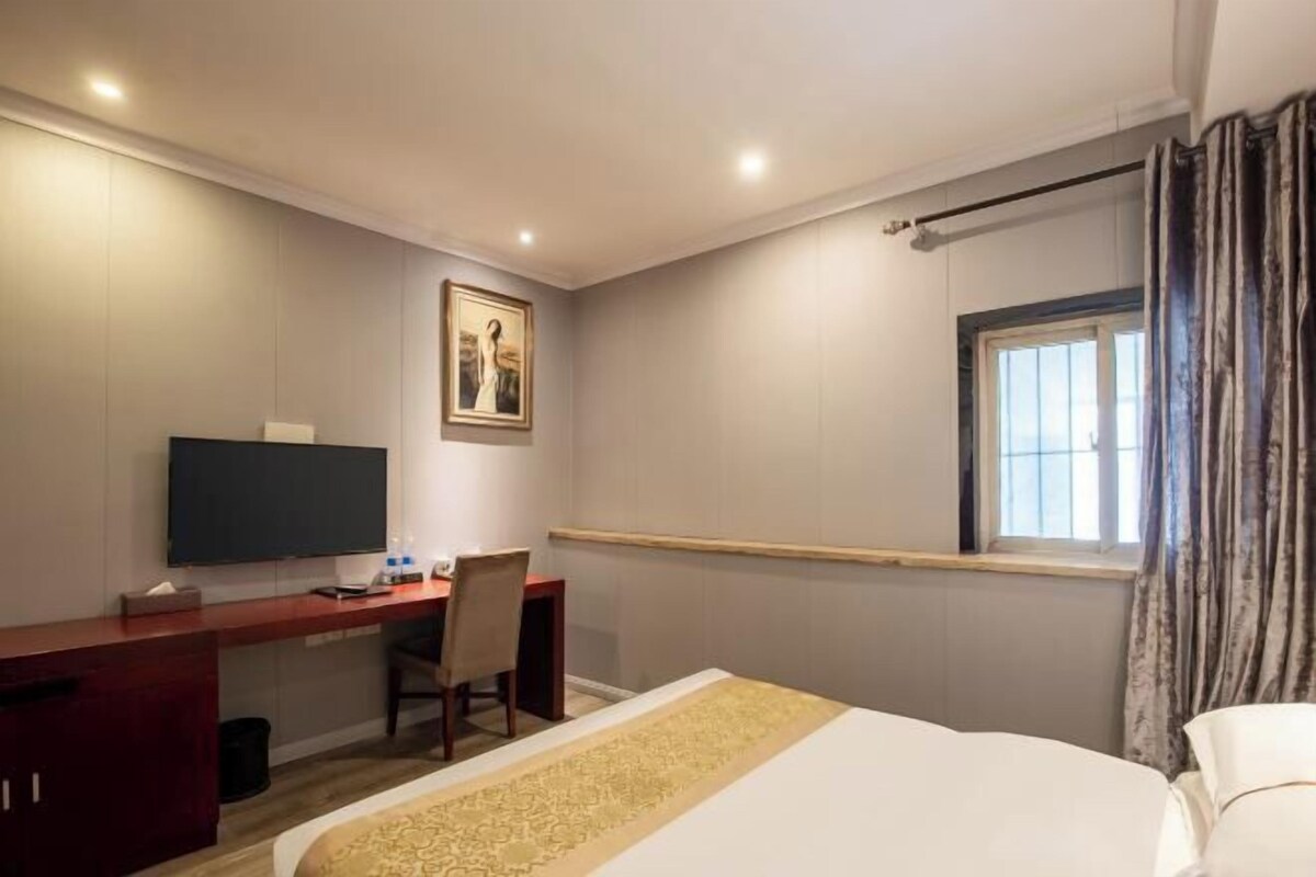 A hotel room with a bed, a desk with a chair, a television, and a window with curtains.