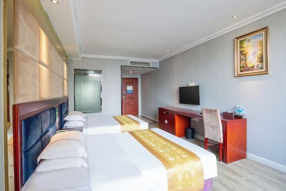 A hotel room with a large bed, a desk, a chair, a television, and a painting on the wall.