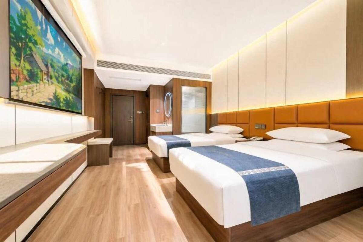 A hotel room with two beds, a large window with a view, a painting on the wall, and a wooden floor.