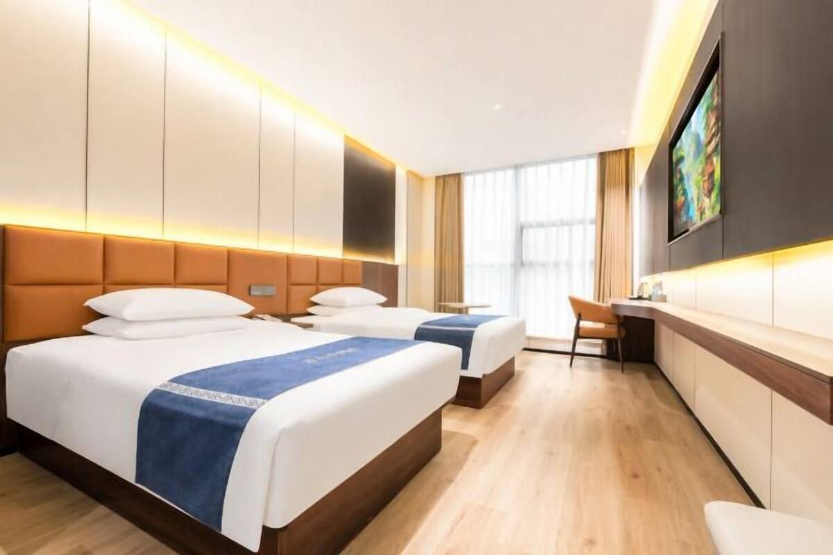A hotel room with two beds, a desk, a chair, and a TV mounted on the wall.