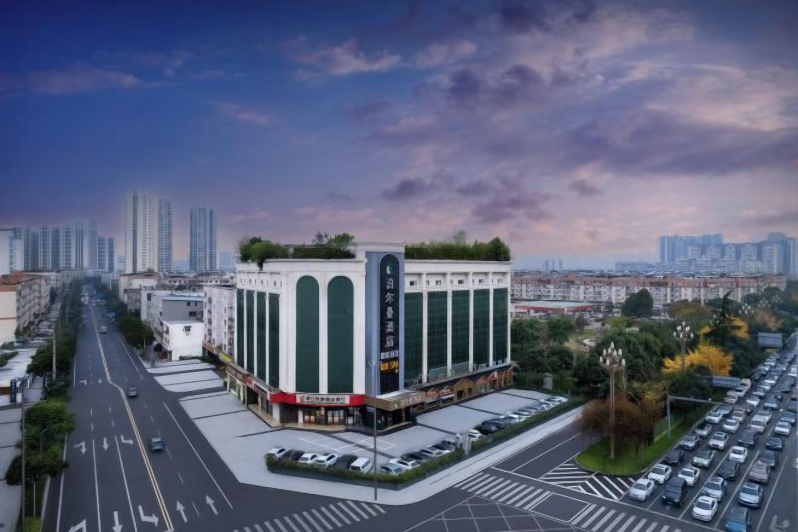 Edifício com vários andares e átrio central, rodeado por um estacionamento e paisagem urbana ao fundo.