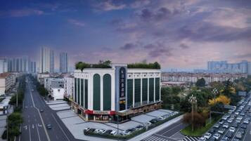 Edifício com vários andares e átrio central, rodeado por um estacionamento e paisagem urbana ao fundo.
