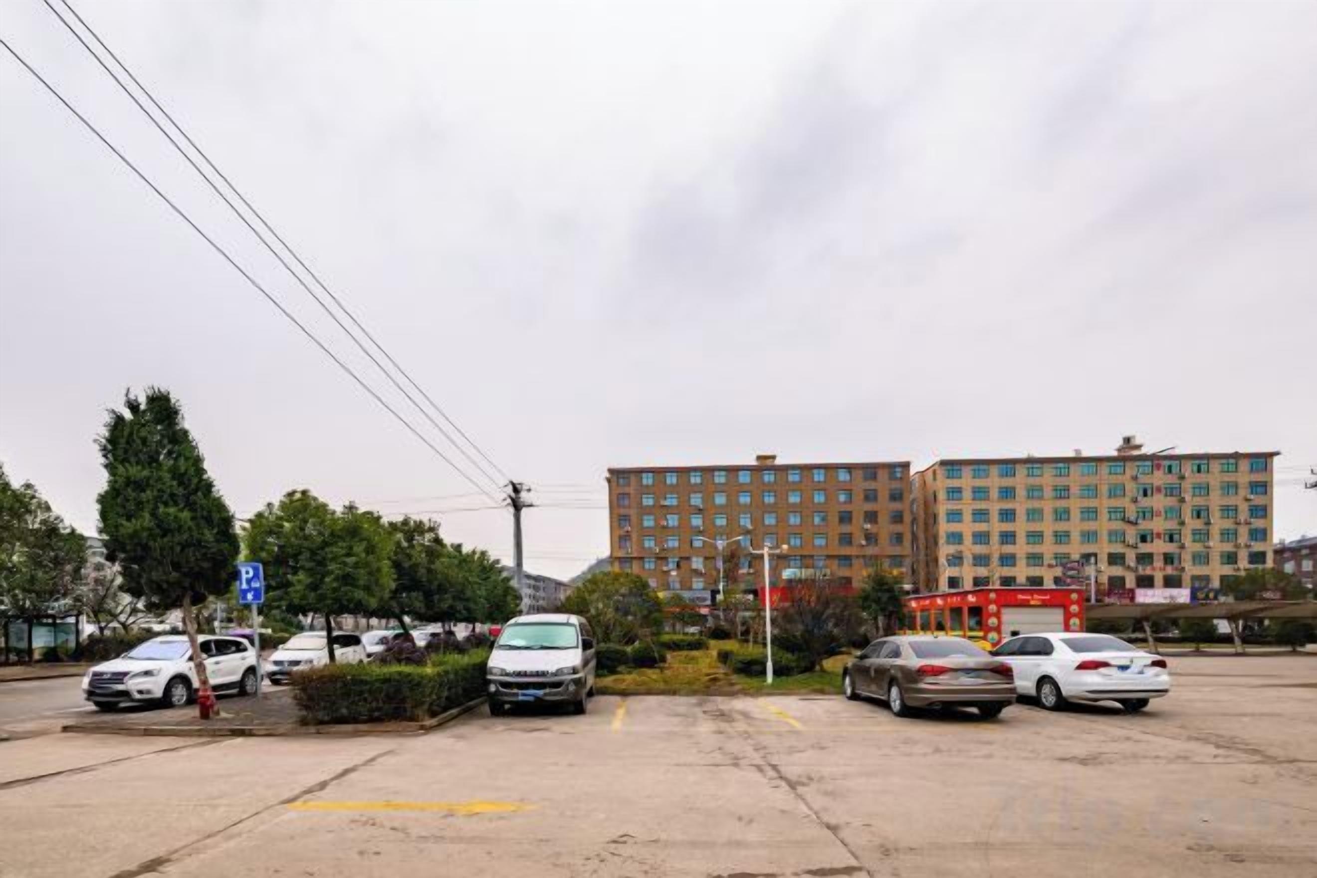Un estacionamiento con varios coches, un edificio al fondo y un letrero azul.