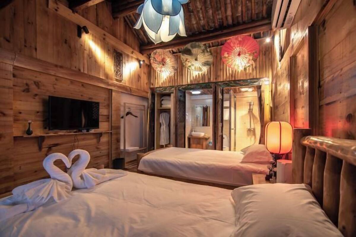 A wooden cabin-style room with two beds, a television, and decorative fans.