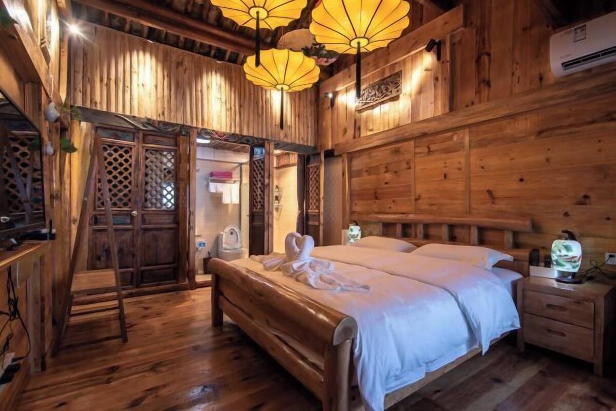 A wooden room with a bed, a nightstand, a ladder, and a door with a lattice design.