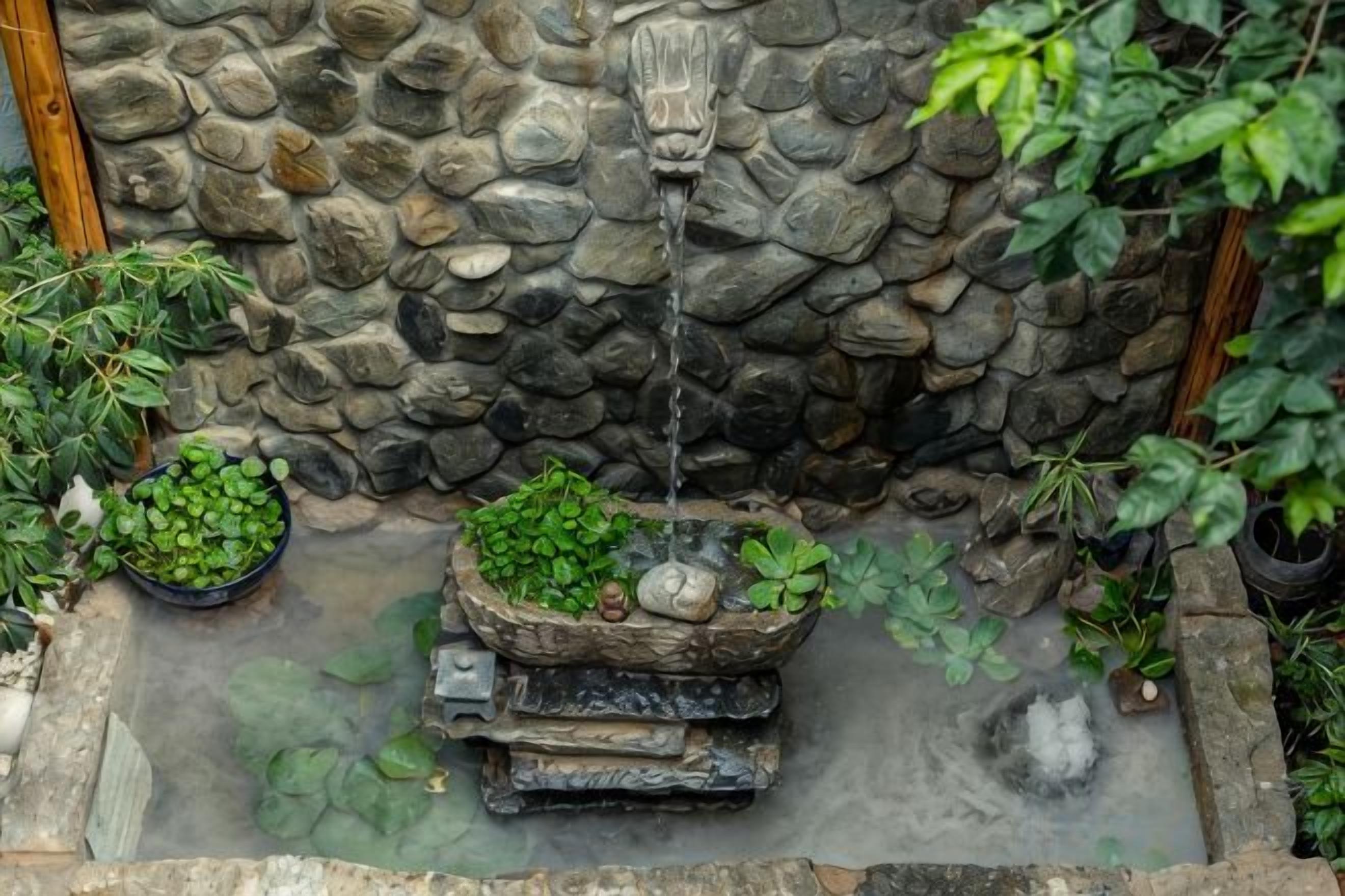 A stone wall with a water feature, including a stone basin and a small waterfall.