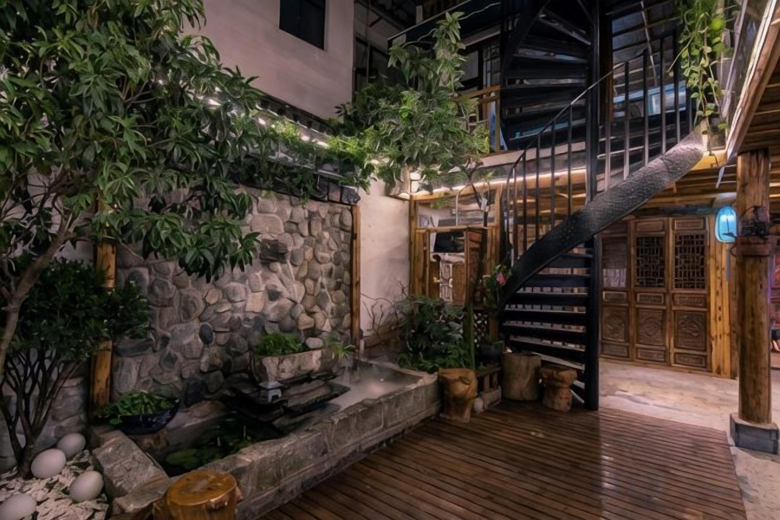 A courtyard with a stone wall, wooden deck, and a staircase leading to a traditional door.