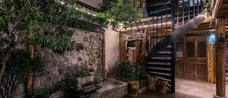 A courtyard with a stone wall, wooden deck, and a staircase leading to a traditional door.
