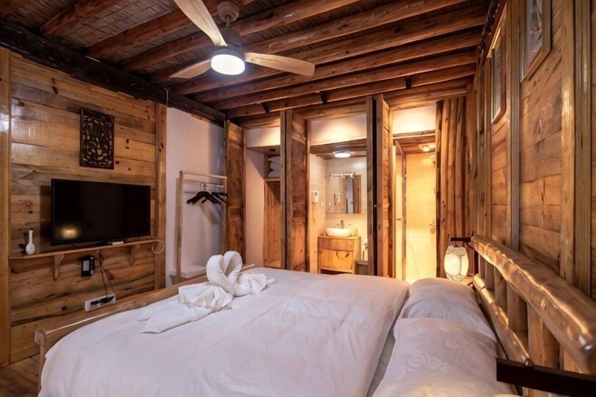 A wooden room with a bed, a television, and a ceiling fan.