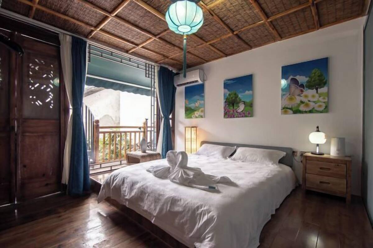 A bedroom with a bed, a nightstand, a wall-mounted lamp, and artwork.