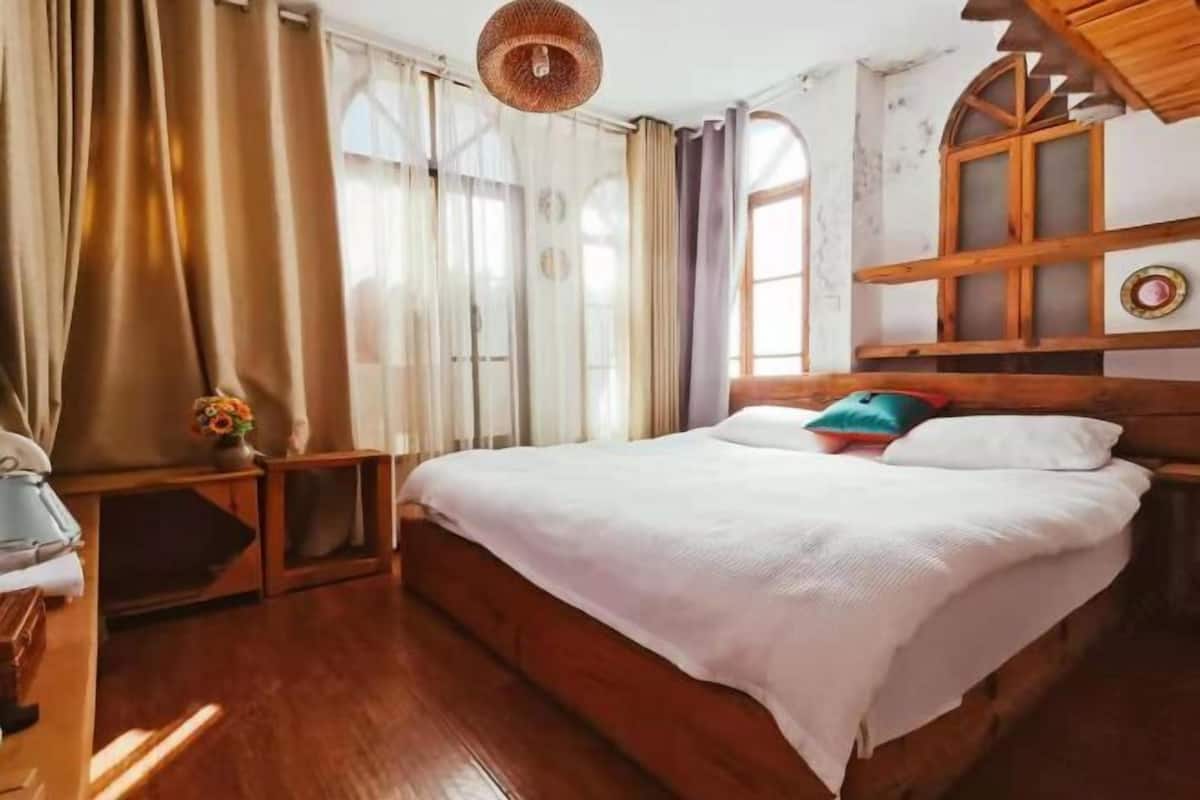 A bedroom with a wooden bed, a bedside table with a lamp, and a window with curtains.