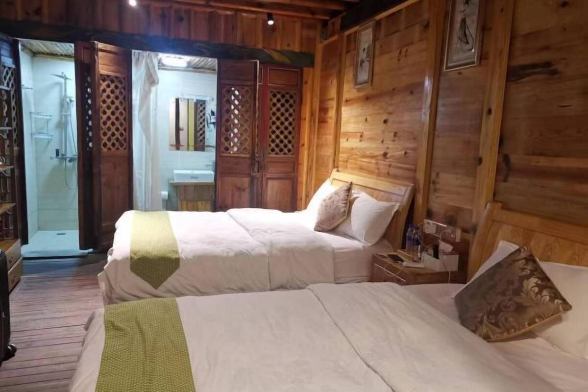 A wooden room with two beds, a shower, and a wooden door.