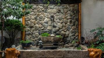 A stone wall with a water feature, surrounded by potted plants and a wooden bench.