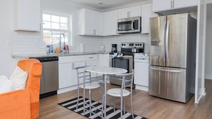 A modern kitchen with white cabinets, stainless steel appliances, and a dining area with a metal table and chairs. - Charming 2-bedroom house with AC and WiFi in enjoyable China Grove (China Grove)