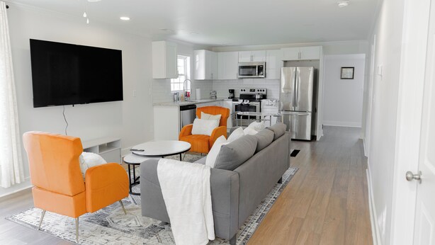A modern living room with a sofa, orange armchairs, and a flat-screen TV. - Charming 2-bedroom house with AC and WiFi in enjoyable China Grove (China Grove)