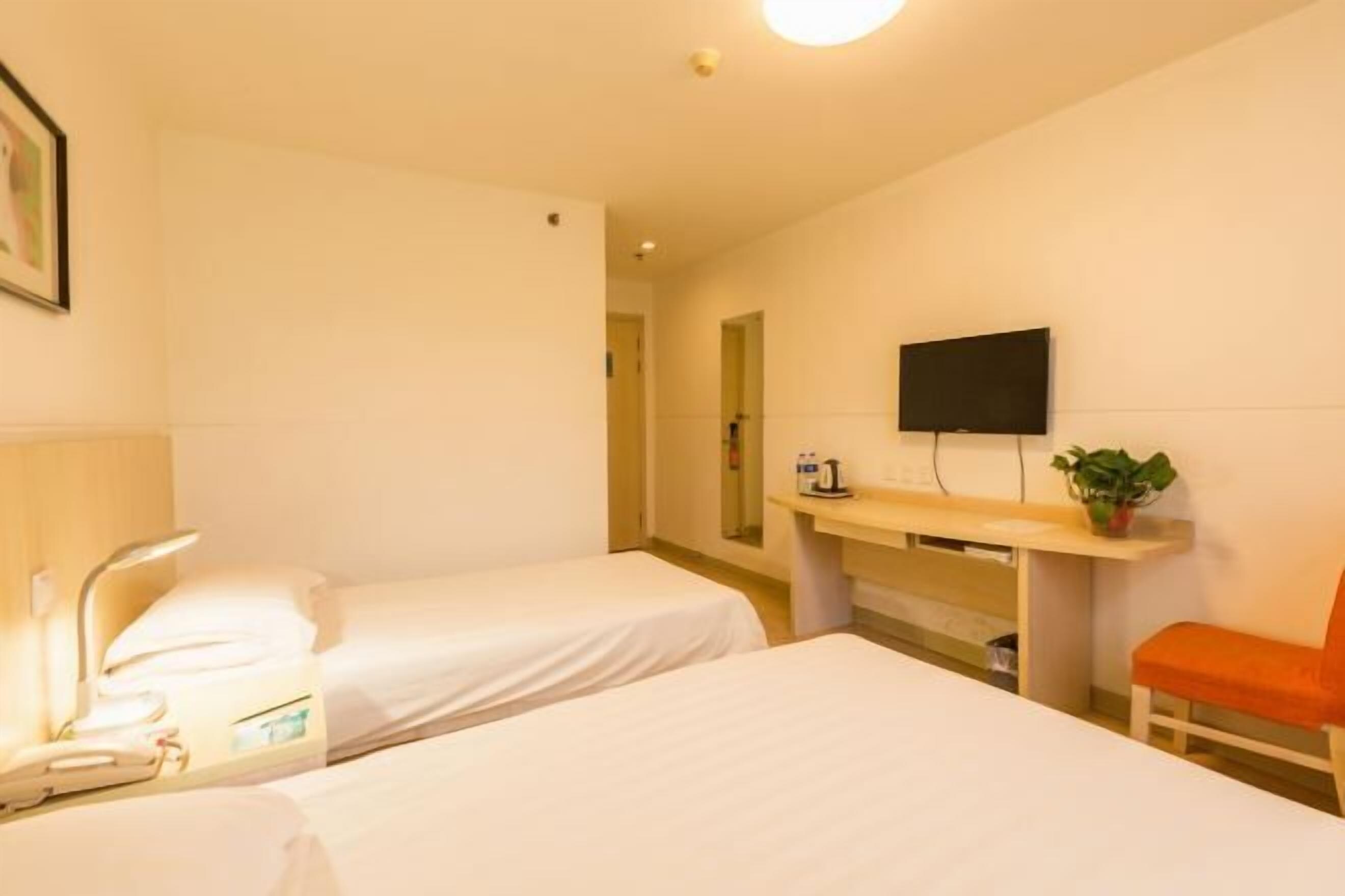 Habitación de hotel con dos camas, un escritorio, un televisor de pantalla plana, una silla y una mesita de noche con lámpara.