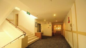 En hotellkorridor med en trappa, heltäckningsmatta och en lång gång som leder till ett annat rum.
