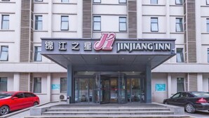 En hotellentrén med en glasfasad, en tydlig skylt med texten ”Jinjiang Inn” och en modern arkitektonisk design.