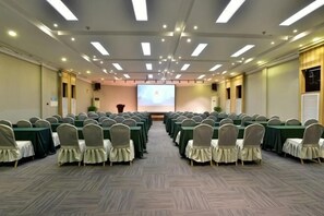 A conference room with rows of tables and chairs, a projector screen, and a podium.