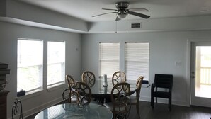 A dining area with a glass table, wooden chairs, a ceiling fan, and large windows. - 3-bedroom house in charming Surfside Beach with AC, WiFi (Surfside Beach)