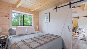 Une chambre dans une cabane en bois, avec un lit, une fenêtre, une porte et un ventilateur de plafond.